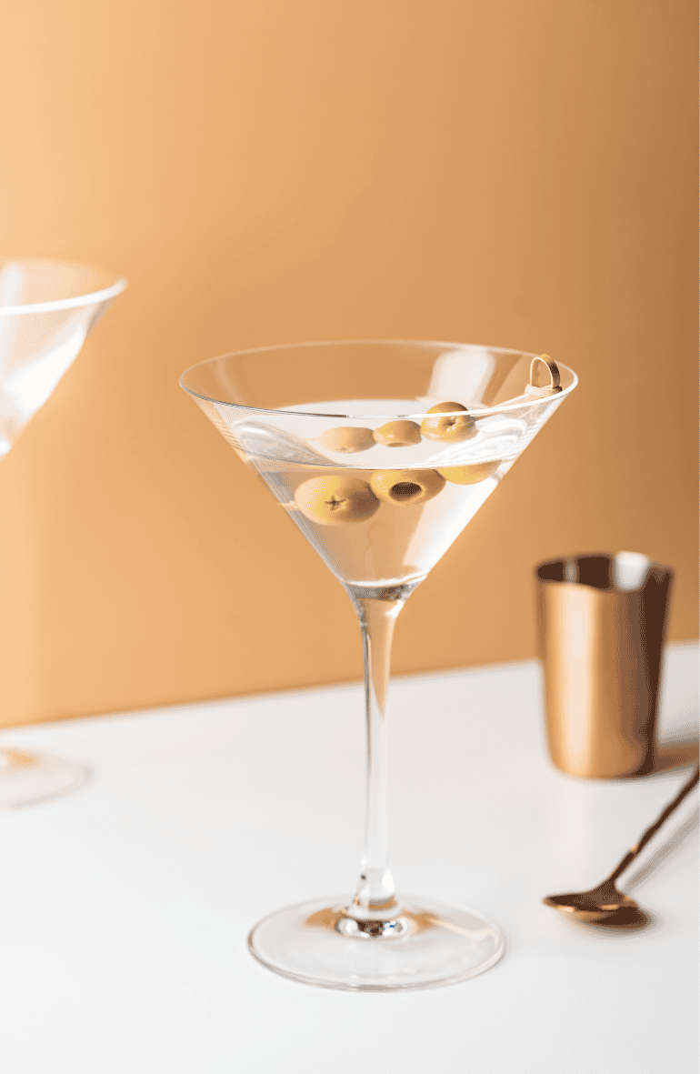 A martini with olives next to bar equipment