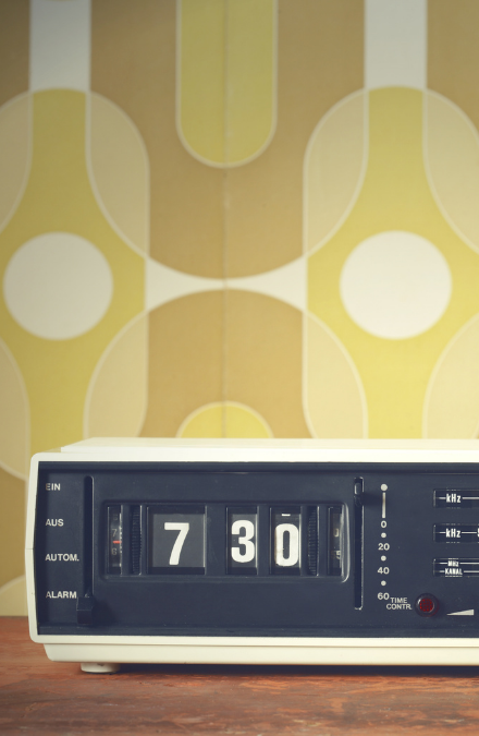 Retro clock radio on a brown dresser in front of yellow and brown patterned wallpaper